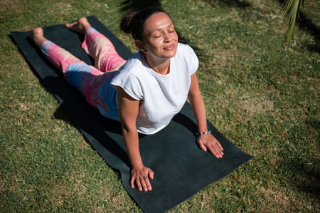 Woman enjoying a yoga session in the sun, doing a cobra pose on a grassy lawn. Relaxes and embraces...