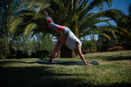 A woman practicing yoga in the park, performing a pose on a mat surrounded by lush green palm trees...