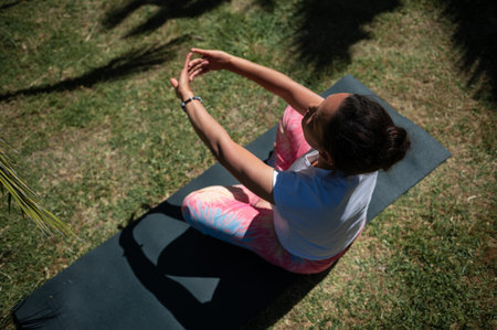A woman performing a yoga pose on a mat in a serene outdoor garden. She is wearing comfortable...