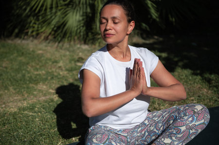 Woman sitting in a meditative yoga pose with eyes closed and hands in prayer position, experiencing...