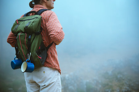 A solo hiker in checkered shirt and outdoor gear is exploring a misty mountain trail with a backpack carrying camping essentials. Perfect for travel, adventure, and exploration themes.の写真素材
