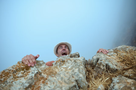 Man experiencing extreme fear while clinging to a rocky cliff. The image captures intense emotions and the adventure and danger of rock climbing in nature.の写真素材