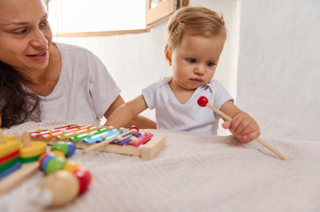 A mother and baby spending quality time playing with a colorful xylophone. The baby is focused while the mother looks on with a smile, featuring family bonding and early childhood development.の写真素材