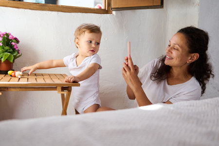 Mother taking a photo of her curious toddler indoors. The scene captures a warm family moment, with...