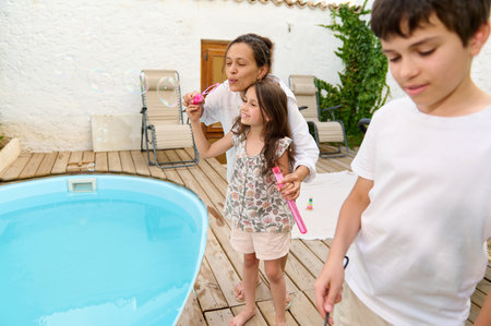 A mother and her children enjoying a sunny day by the pool, blowing bubbles and having a fun time...