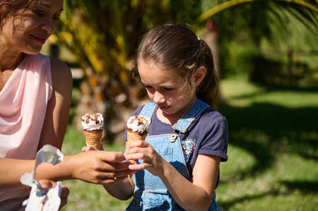 A mother and daughter sharing a sweet moment together with ice cream cones at a park on a sunny day....