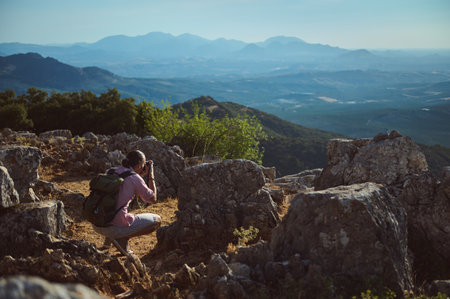 A photographer takes pictures in a rocky mountain landscape during daytime. The clear blue skies and vast mountain range in the background create a stunning nature scene.の写真素材