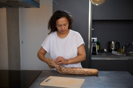 Woman unwrapping a loaf of bread in a modern kitchen setting, preparing for a meal. Focus on...