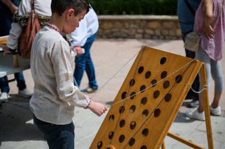 Young boy engaged in a fun outdoor wooden game on a sunny day. The scene showcases a public event...