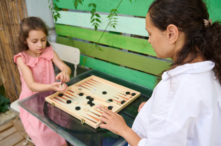 Mother and daughter enjoying quality time together playing backgammon in a serene outdoor setting....
