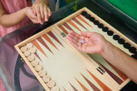 A family enjoying quality time playing backgammon at home. Hands of adults and children engaging in...