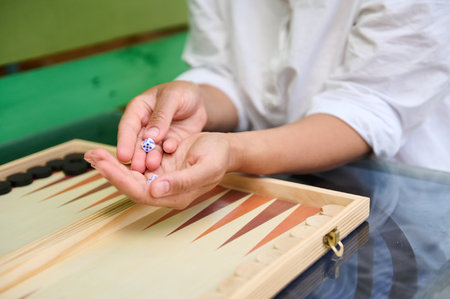 Close-up of hands holding dice, preparing to roll while playing backgammon on a wooden board. The...
