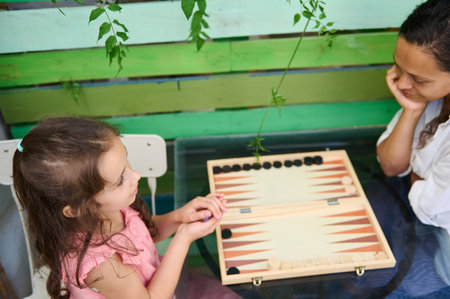 A mother and daughter enjoy a bonding moment while playing a game of backgammon at home. Family time and leisure meet in this playful, cozy scene.の写真素材