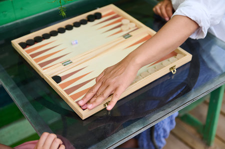 Close-up of two people playing backgammon on a glass table. Hands moving pieces on the board....