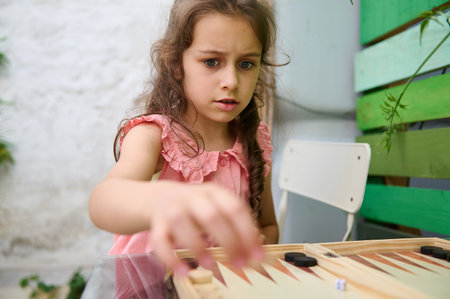 A young girl intently playing a board game outdoors. She appears concentrated as she makes her move....