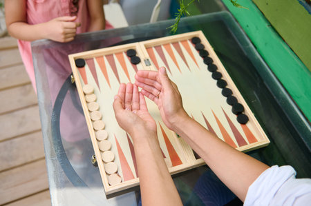 Close-up of two people playing backgammon outside on a glass table. Fun, relaxation, and leisure...