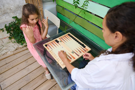 A heartwarming moment of a mother and daughter playing backgammon together in a cozy outdoor garden, fostering family bonding and fun.の写真素材