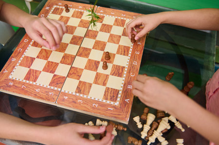 Children's hands seen playing a chess game on a wooden board. They organize pieces, enhancing...