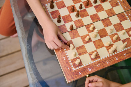 Top view of two individuals engaged in a chess game on a glass table, focusing on strategy and...