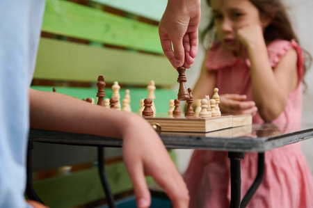 Two children intensely playing an outdoor chess game. The boy and girl are concentrating on the current moves, showcasing strategy and intelligence in a playful setting.の写真素材