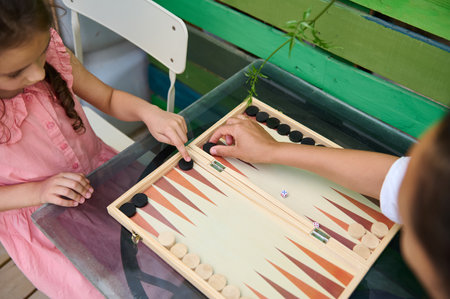 A child and adult enjoying a game of backgammon outside. The casual setting and shared activity...