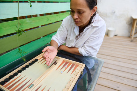 A woman in a casual white shirt plays backgammon on a glass table outdoors, conveying relaxation and leisure.の写真素材
