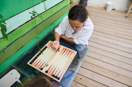 Woman enjoying a game of backgammon on a wooden patio. Relaxed outdoor setting focused on strategic gameplay and leisure activities.の写真素材