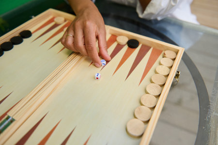 Close-up of a hand rolling dice on a wooden backgammon board, showcasing strategy and entertainment...