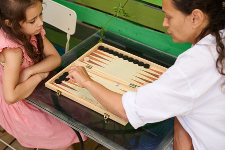 A mother and her young daughter enjoying a game of backgammon at home. Family bonding and quality...