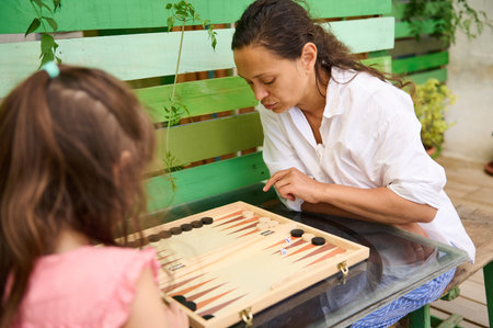 A mother and daughter enjoying a game of backgammon outdoors. The image captures the essence of...