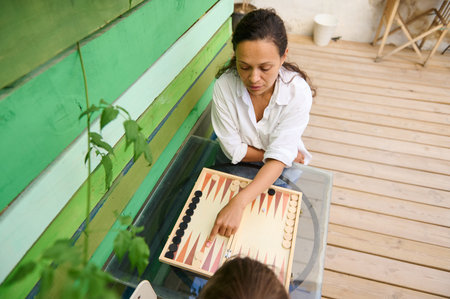 Woman enjoying a game of backgammon on her wooden deck. Relaxed and casual outdoor setting. Female...