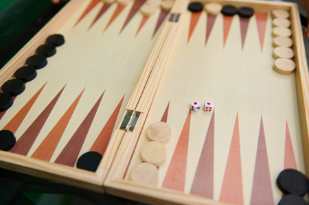 Close-up of a traditional wooden backgammon board, featuring black and white pieces and two dice,...