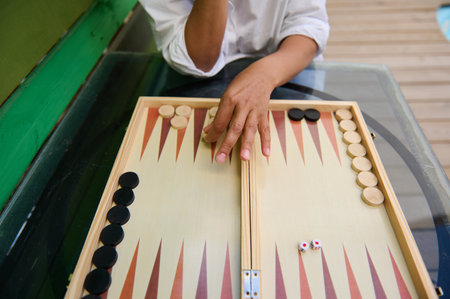 A close-up shot of a person playing backgammon on a wooden board. The game is set outdoors on a glass table, creating a fun and relaxed atmosphere.の写真素材