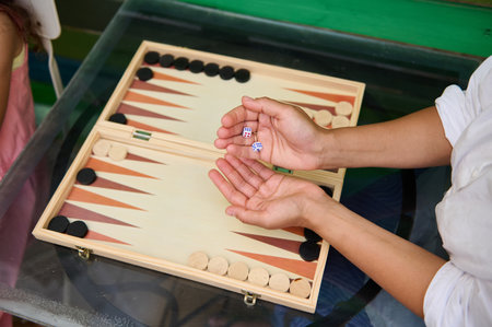 Two people enjoying a game of backgammon on a glass table. One player is holding dice, creating...