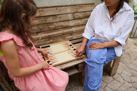 Mother and daughter spending quality time together playing a game of backgammon outside. The image...
