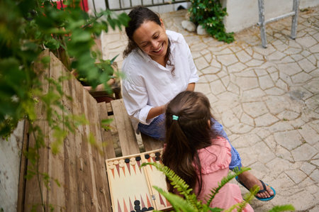 A mother and daughter sharing a joyful moment while playing backgammon outside in a serene setting....