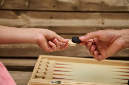 Close-up of two hands exchanging black and white checkers pieces during an outdoor backgammon game....