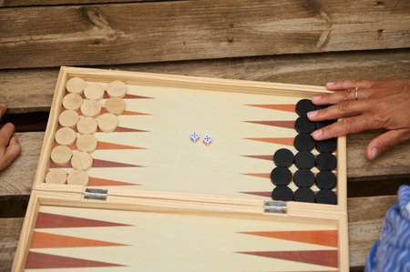 Close-up of two people playing a game of backgammon on a wooden board with dice, situated on a...