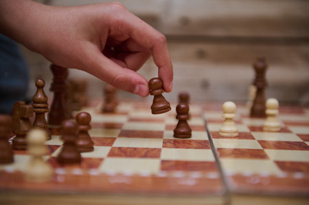Detailed shot of a hand strategically moving a chess piece on a wooden board, highlighting skills in...