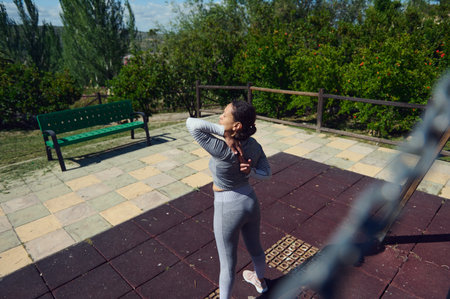 A woman in athletic wear stretches in a tranquil park setting, promoting wellness and fitness amidst...
