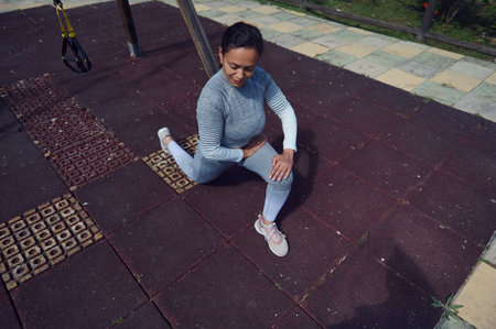 A woman wearing athletic clothing stretches on a workout mat outdoors, getting ready for physical...