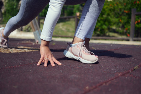 Athlete's feet and hands poised for a sprint on a track, representing readiness, fitness, and a...