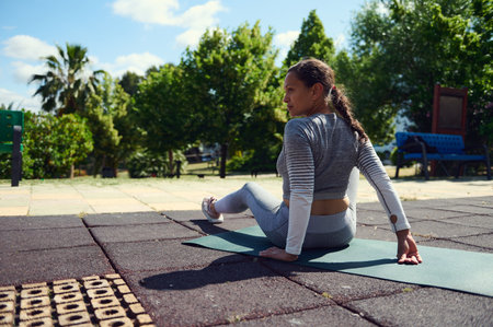 A woman in athletic wear practices yoga outside on a mat. Perfect for concepts of relaxation,...