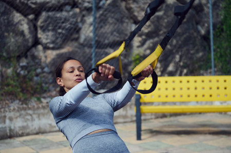 Woman performing a TRX workout outside, emphasizing strength and fitness. The scene includes a...