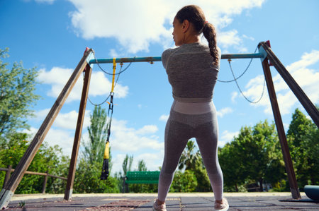 A woman in sportswear stands in a playground, getting ready for an outdoor workout under a bright,...