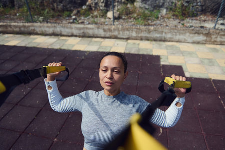 A determined woman engages in suspension training outdoors, utilizing resistance straps for a full...