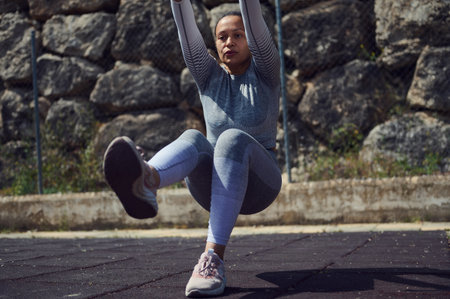 Focused woman in athletic wear performing an outdoor workout against a rocky backdrop, illustrating...