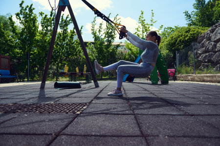 A woman in athletic attire works out with resistance bands in a park, focusing on strength and...