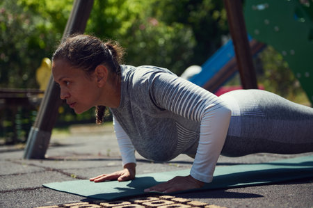 A determined woman performs a push-up outdoors, emphasizing fitness and healthy lifestyle. Captured...