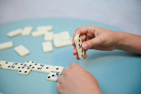 Close-up of hands playing dominoes on a blue surface, highlighting strategy, focus, and tactile...